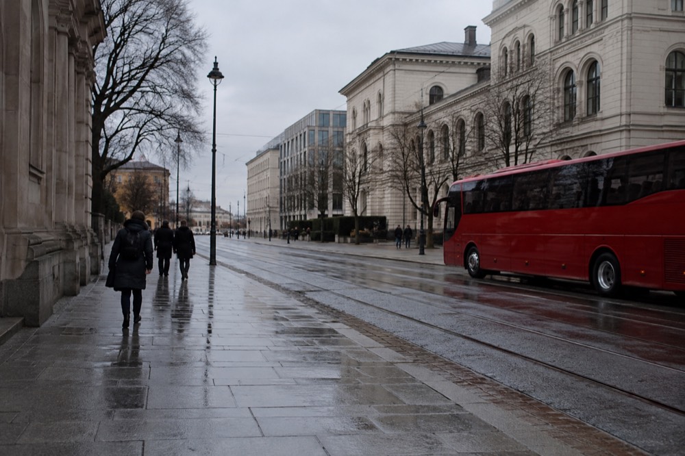 Red sightseeing bus parked on a wet Oslo street near museum buildings