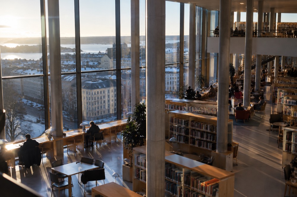 Modern library interior with tall atrium and visitors reading under warm light