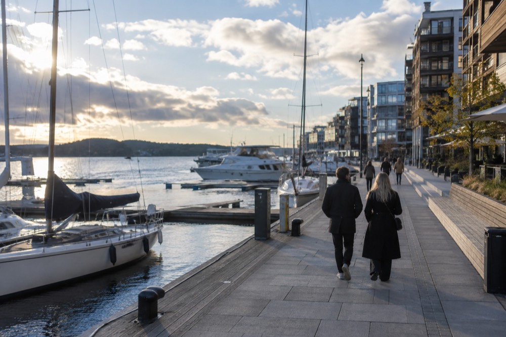 A couple walking the waterfront promenade at Aker Brygge with boats moored along the pier