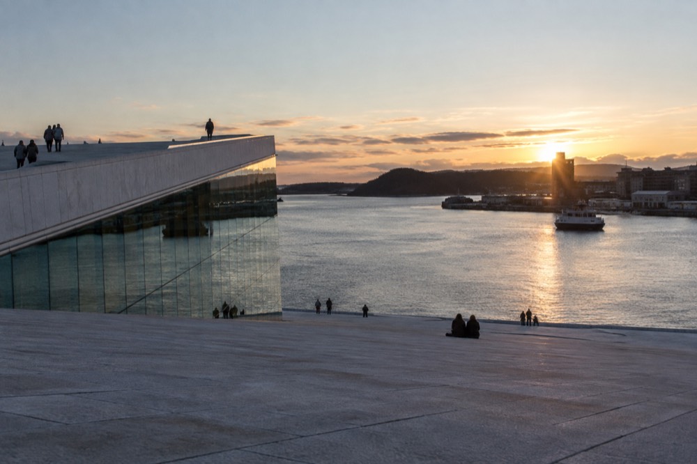 The sloping marble roof of the Oslo Opera House at sunset with the fjord beyond