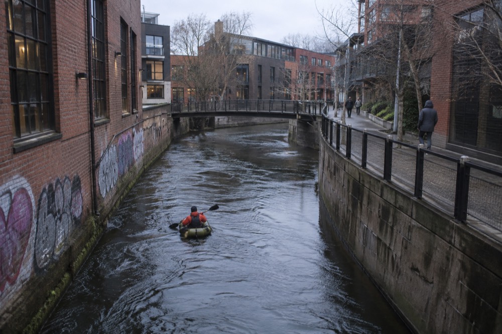 A packraft floating down the Akerselva river between graffiti-covered walls