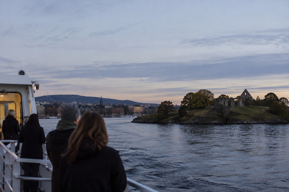 A small ferry approaching a green island with a ruined stone abbey
