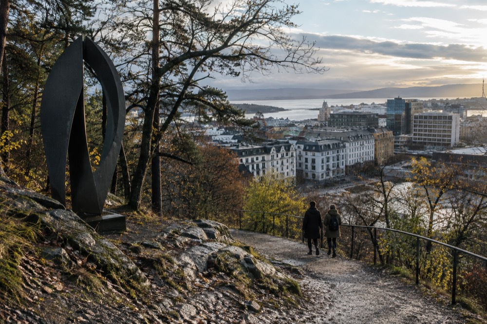A forested hillside trail with a large modern sculpture beside it