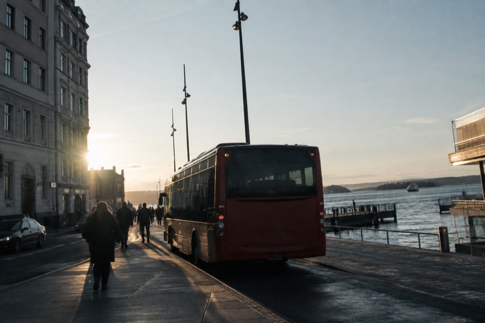 A city bus parked beside a fjord pier with islands in the distance