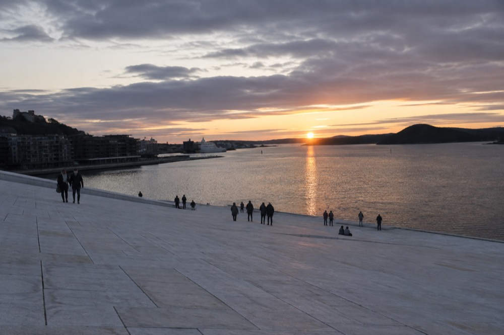 The sloping marble roof of the Oslo Opera House at sunset with the fjord behind